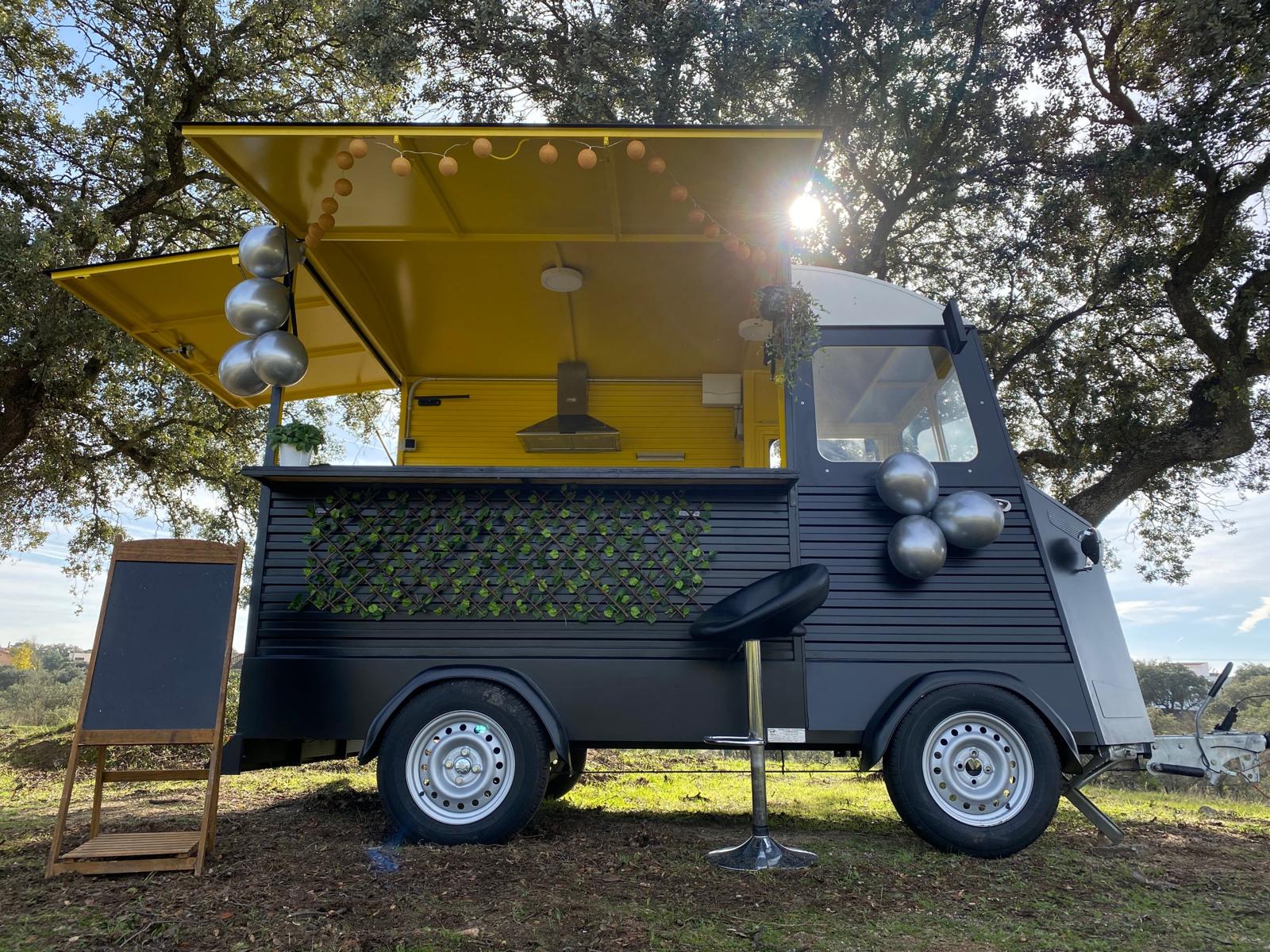 El food truck de MadTruck, negro con el interior amarillo mostaza, abierto y decorado para un evento